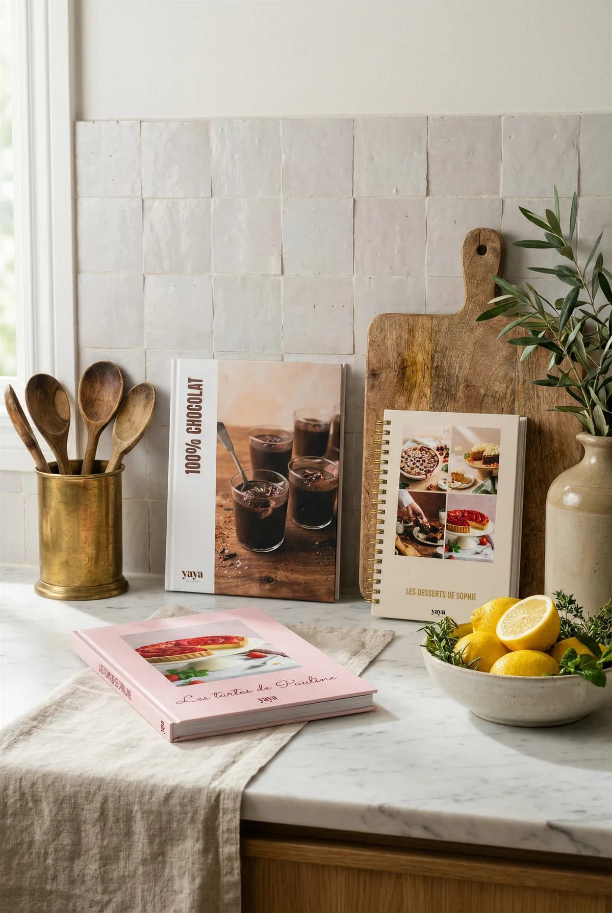 La collection de livres de recettes YAYA mise en scène sur un plan de travail · 100% Chocolat, Les Desserts de Sophie et Les Tartes de Pauline